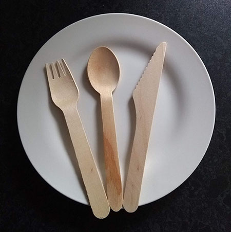 A wooden spoon, a wooden fork, and a wooden knife on a plate.