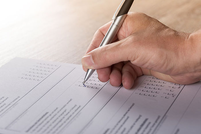 A hand is shown holding a pen as it ticks off a box on a survey sheet.