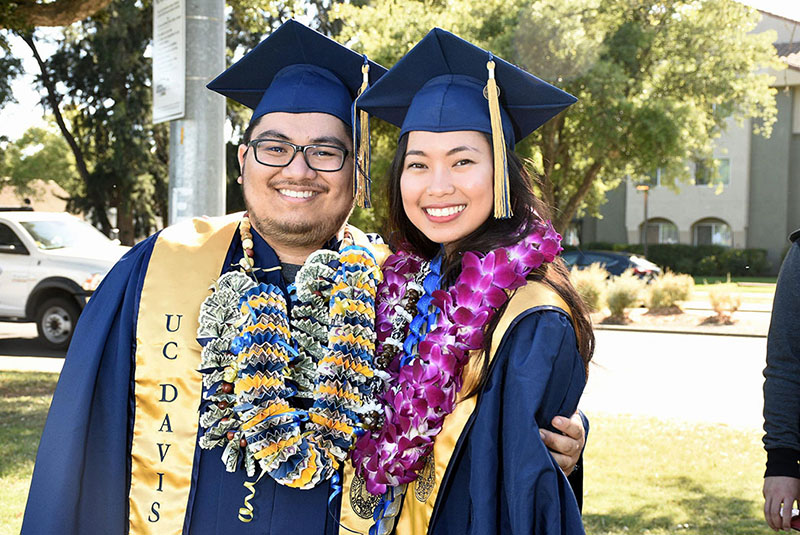 A young man and a young woman are standing next to each other wearing graduation caps and gowns.