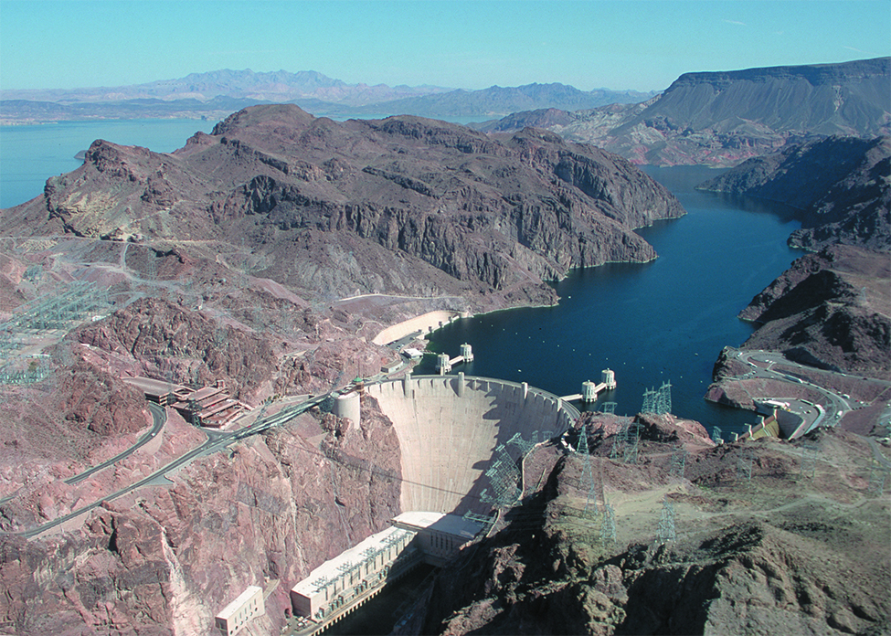 Esta é uma foto da Represa Hoover. A imagem mostra a barragem ao fundo e a água corrente em primeiro plano abaixo da barragem.