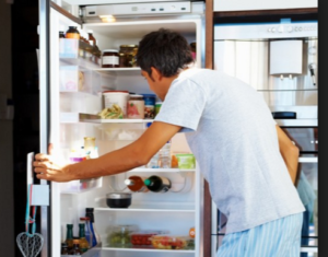 Person standing at open refrigerator full of food.