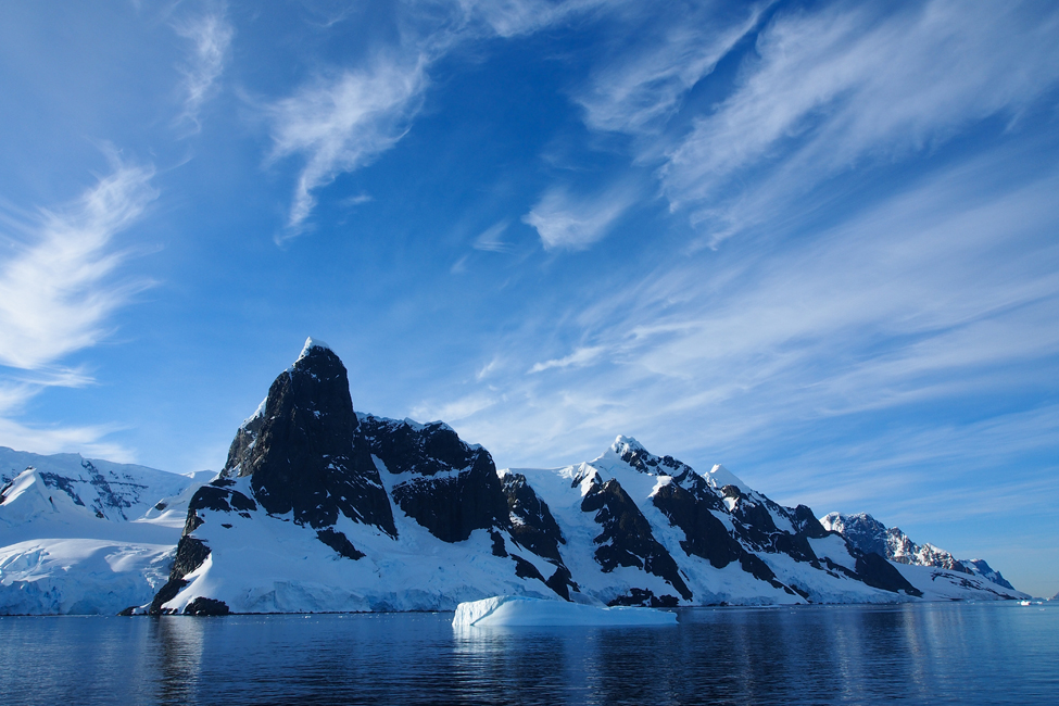 Imagen de la Antártida mostrando el agua, la montaña y los picos de iceberg bajo un cielo azul brillante